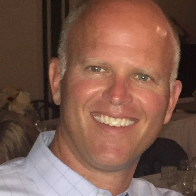A smiling man with short grey hair, wearing a checkered shirt.