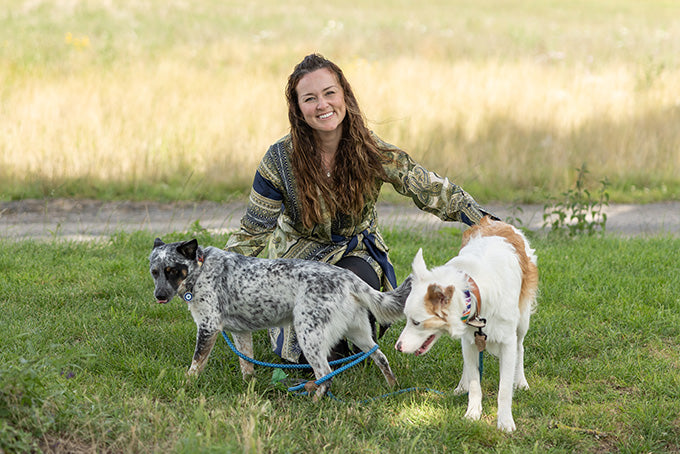 This image is of Courtney Miller, Chief Veterinary Officer at YuMOVE, with two dogs on leashes, with two dogs, one speckled and one white with brown spots, on a grassy field.