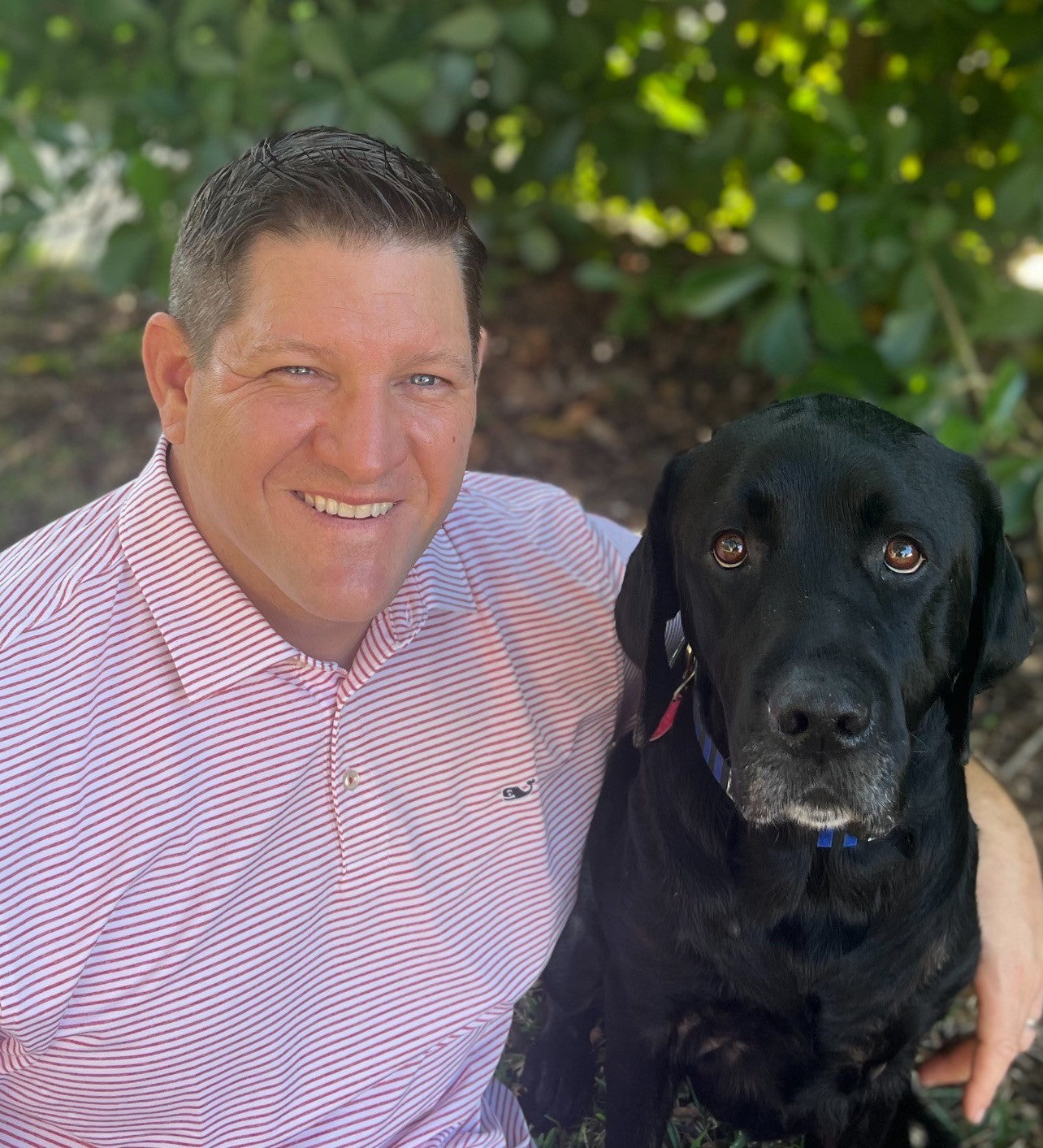 The image is of Dan Downs, National Veterinary Sales Manager at YuMOVE, with a black dog in front of a leafy green background.
